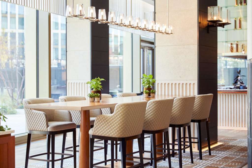 Modern meeting space with high-top table, quilted bar seating, floor-to-ceiling windows, and contemporary pendant lighting.