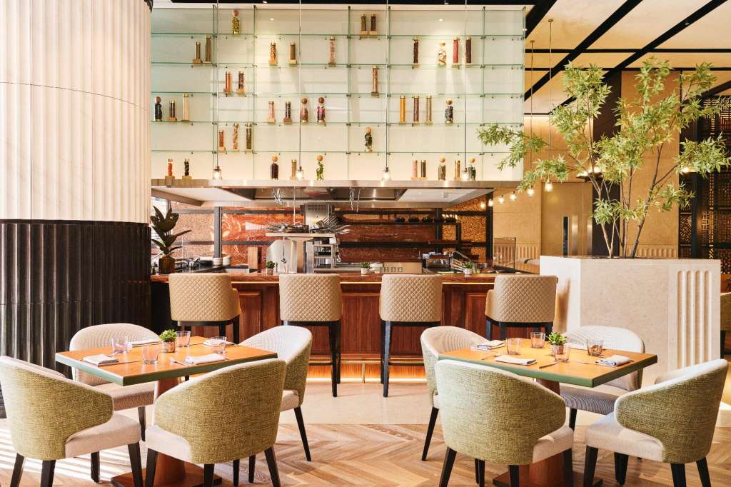 Private dining space with two tables set for service, bar seating, and floor-to-ceiling shelving displaying bottles.