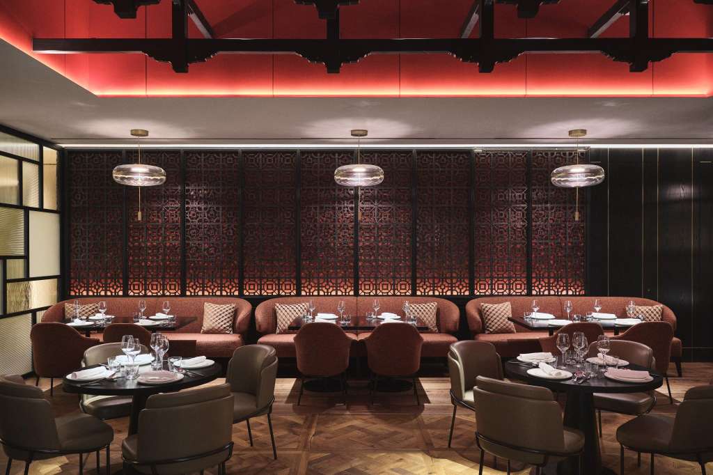 Semi-private dining area with burgundy banquettes, round tables, modern pendant lighting, and geometric wall panels.