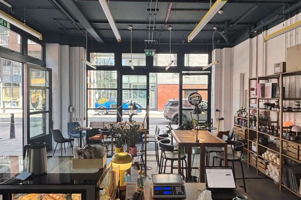 Modern café interior with industrial ceiling, display case, counter seating, and street-facing windows.