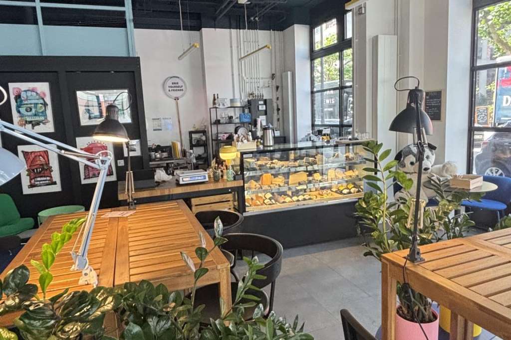 Modern café interior with wooden tables, potted plants, pendant lighting, and pastry display counter.