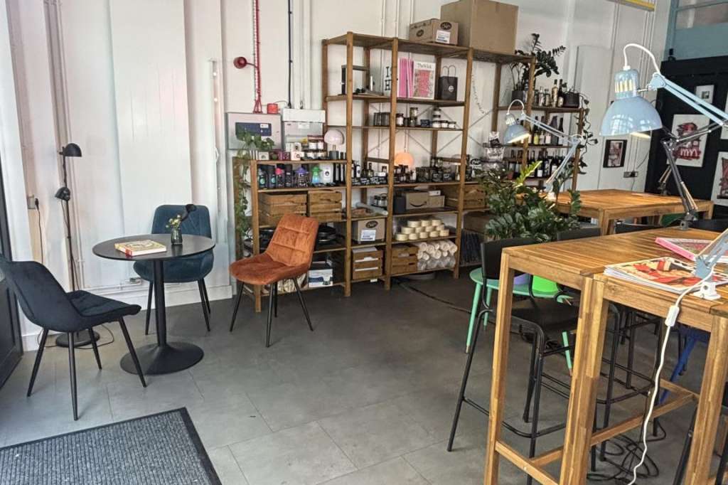 Industrial warehouse space with exposed ceiling, wooden tables, shelving units, and casual seating arrangement.