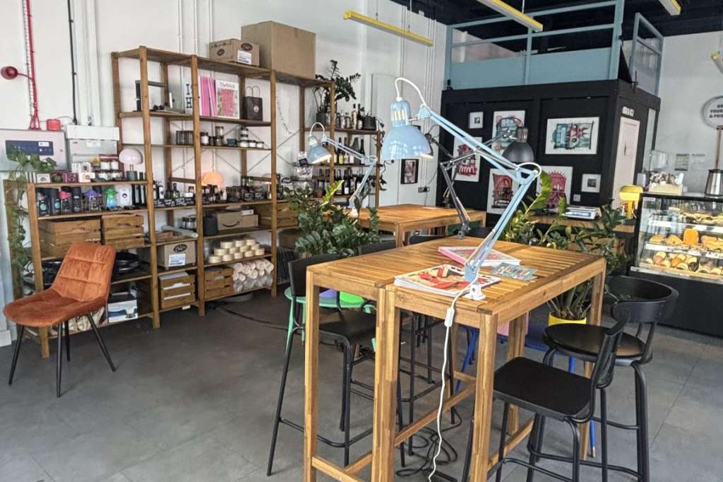 Industrial-style interior space with wooden high-top tables, orange chairs, shelving, and modern pendant lighting.