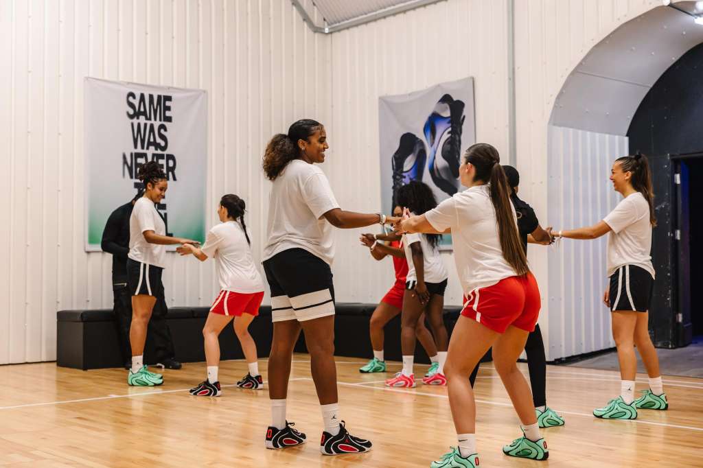 Group of people in athletic wear participating in a team-building exercise in a modern industrial space with motivational wall graphics.