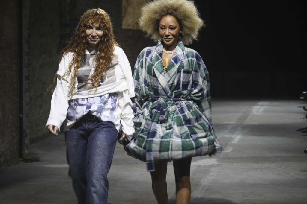 Two models walking down an industrial corridor with exposed brick walls and overhead lighting.