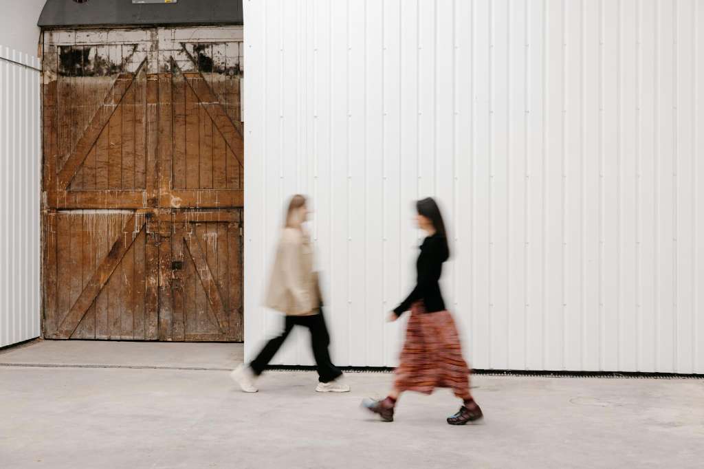 Exterior urban space with weathered wooden doors and white corrugated walls. Two people walking.