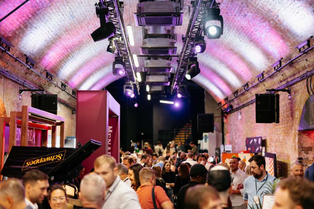 Industrial brick venue with arched ceiling, pink and purple lighting, crowd of guests, and stage setup.