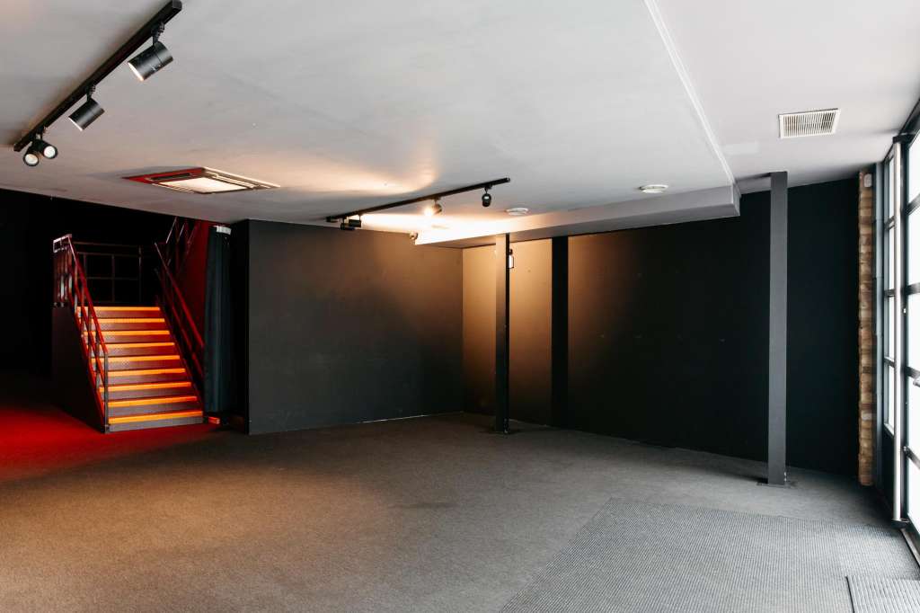 Large open event space with dark walls, track lighting, red staircase, and polished concrete flooring.