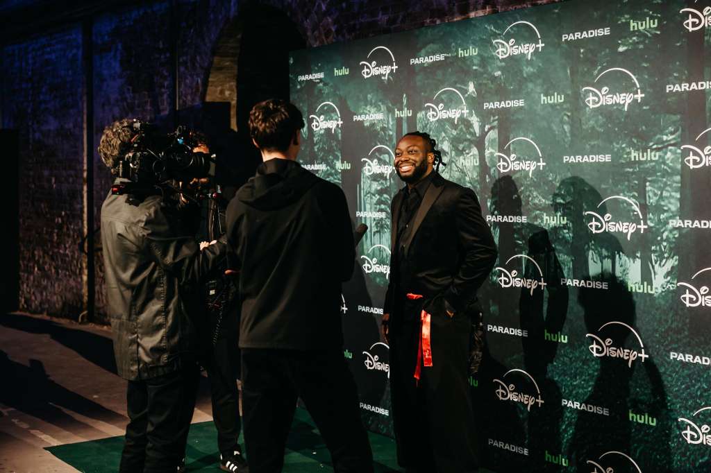 Red carpet event with branded backdrop featuring Disney+ and Hulu logos, guests and camera crew present.
