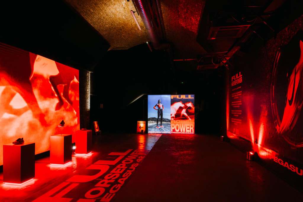 Industrial space with red ambient lighting, video screens displaying product imagery, and illuminated display elements.