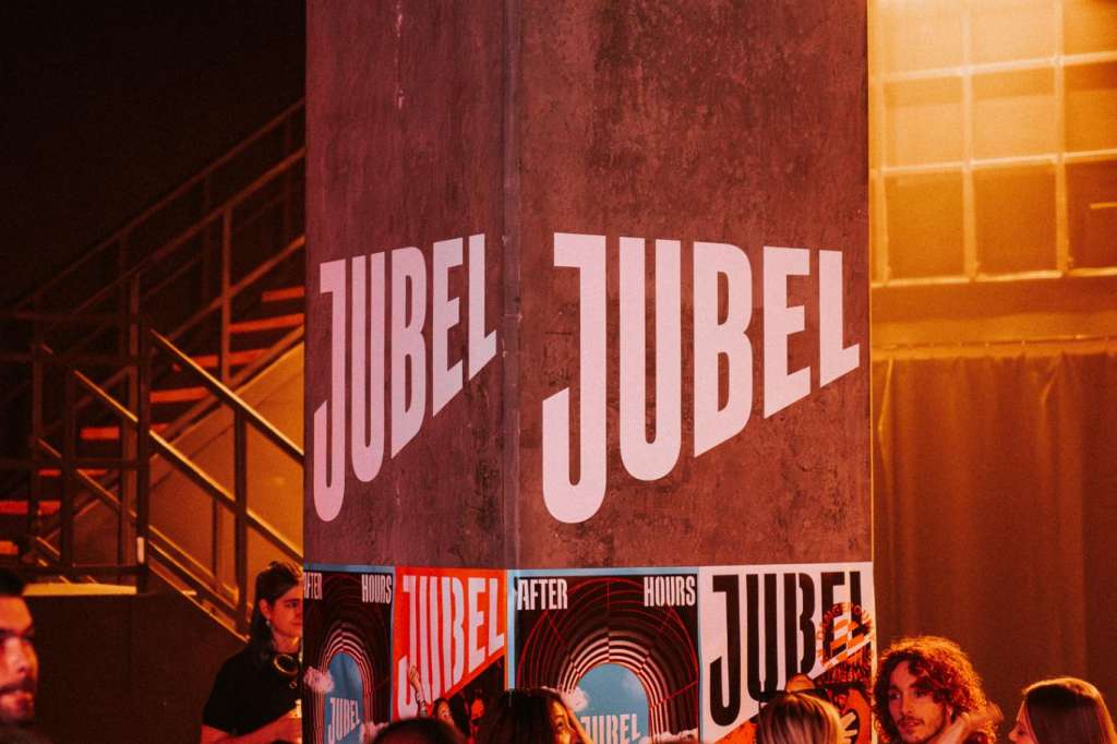 Industrial venue space with red and orange lighting, large branded signage, and guests mingling during an event.