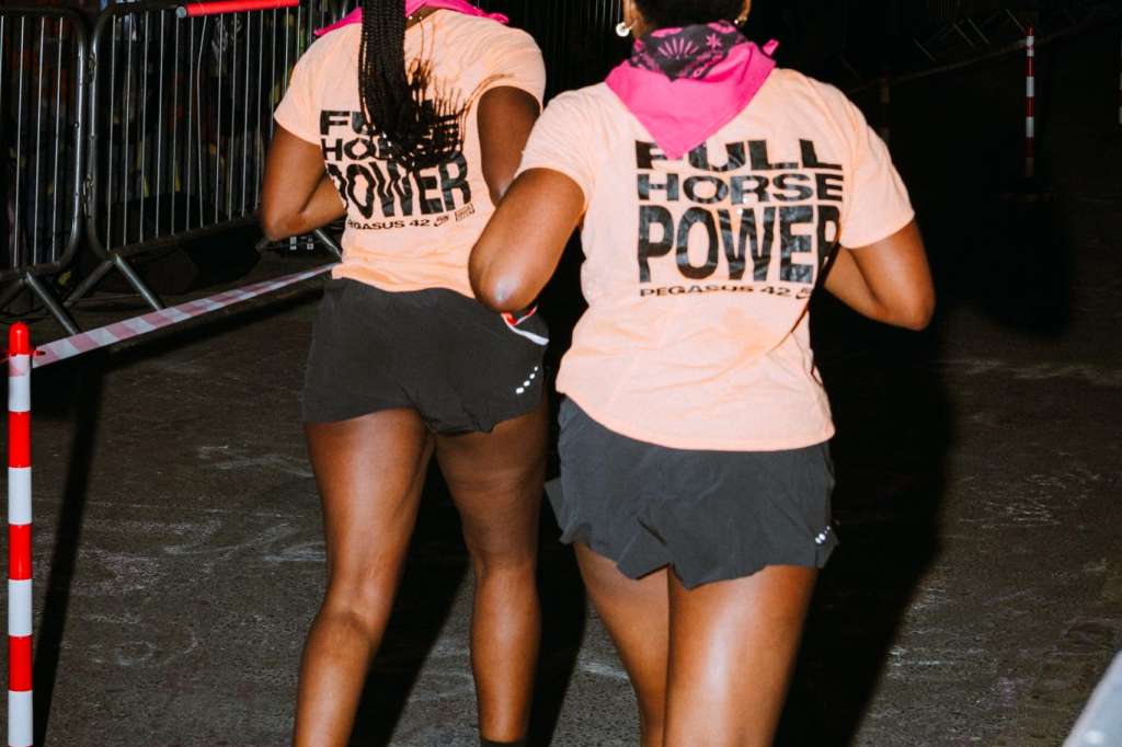 Two runners in matching pink shirts participating in an organized race event on an urban street with graffiti walls.