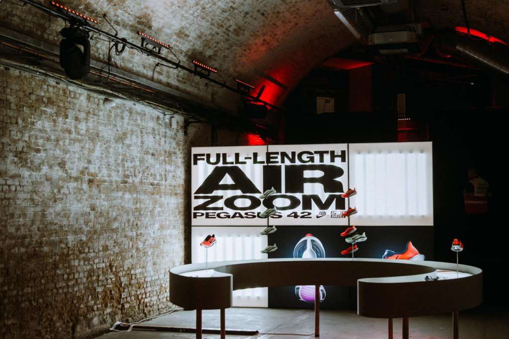Industrial brick space with curved display tables, large signage, and red accent lighting for exhibition setup.