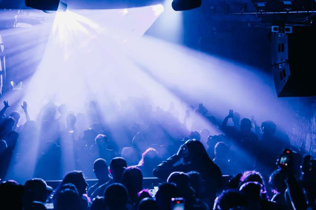 Large crowd under dramatic blue stage lighting with professional spotlights and atmospheric fog effects.