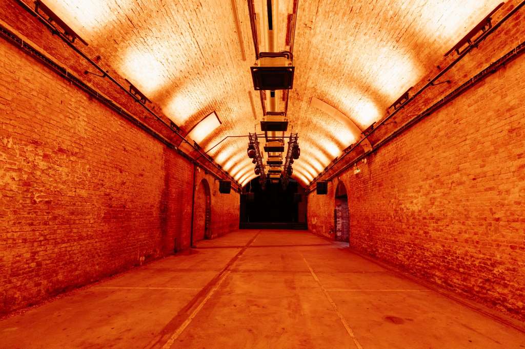 Industrial brick tunnel with arched ceiling, linear uplighting, and polished concrete floor.