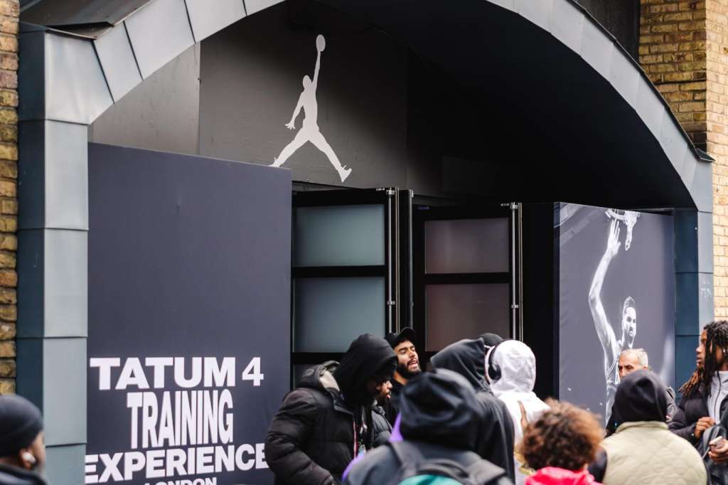 Exterior entrance with crowd queuing at branded pop-up experience featuring athletic imagery and signage.