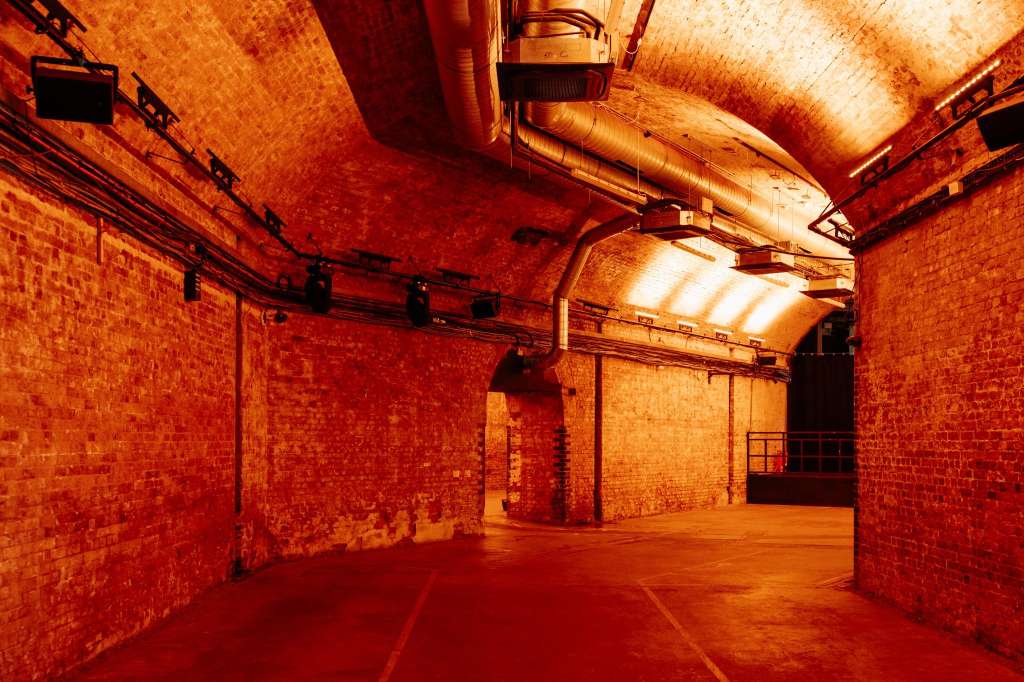 Industrial brick space with red ambient lighting, exposed ductwork, and polished concrete floor.