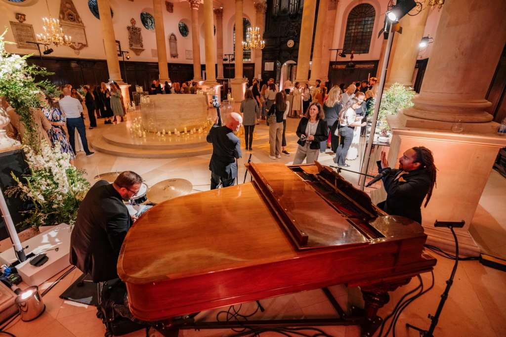 The Nave set up for an evening reception with a grand piano, candlelit circular bar, and guests mingling under warm lighting.