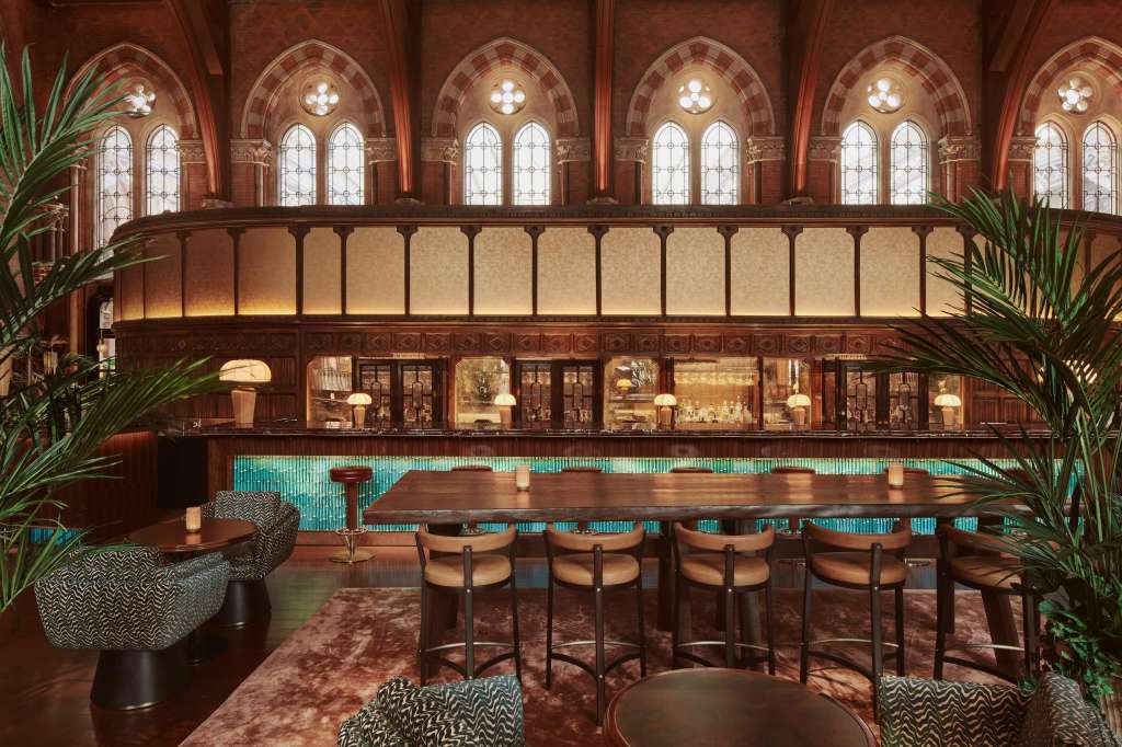 The Booking Office bar with long wooden counter, arched windows, ornate red-brick architecture, and turquoise tile accents.