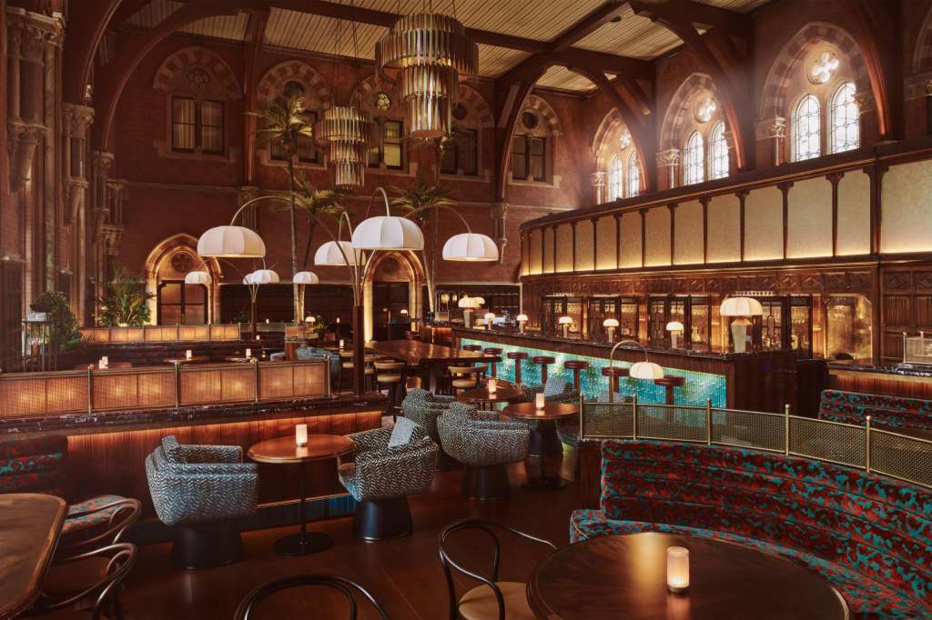 The Booking Office with arched brick architecture, pendant lighting, round tables with upholstered seating, and ornate railings.