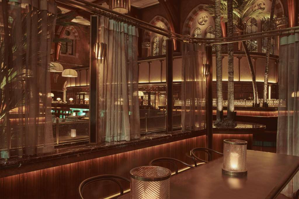 The Booking Office bar with high counter seating, warm ambient lighting, and arched architectural details visible through windows.