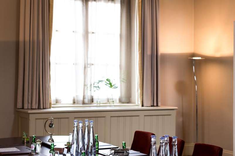 Hansom Hall set up for a meeting with long dark table, burgundy chairs, water bottles, and pendant lighting.