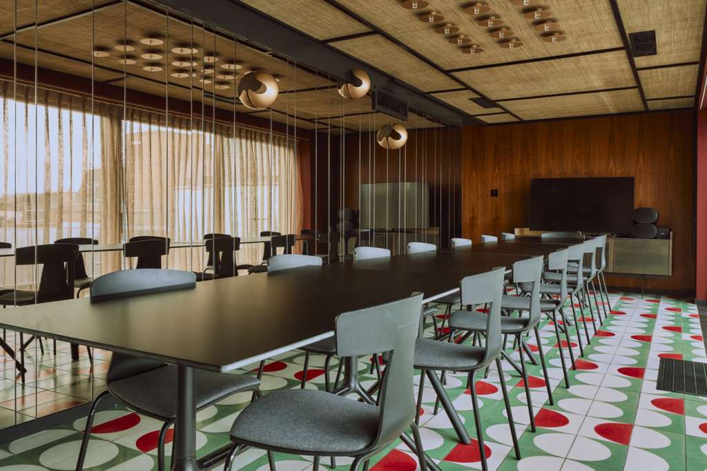 Modern conference room with long black table, light blue chairs, geometric patterned flooring, and pendant lighting.
