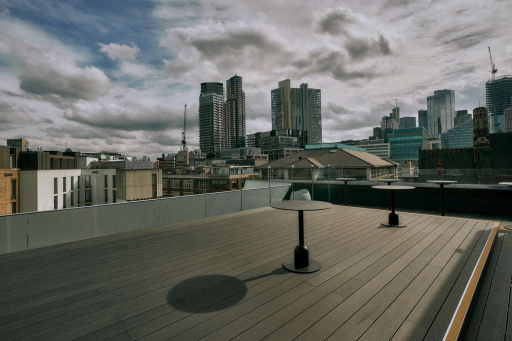Rooftop terrace with composite decking, metal railings, and London skyline views. Two black umbrellas visible.