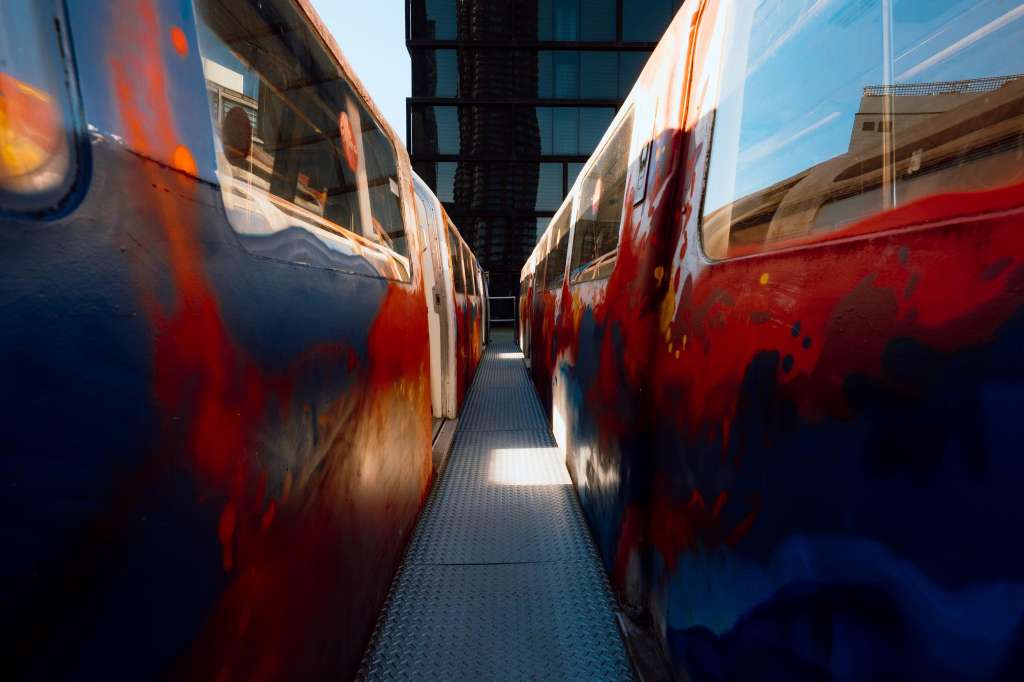 Exterior view of red and blue trains parked between urban buildings under clear sky.