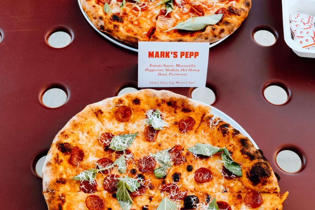 Two pizzas on a burgundy surface with circular cutouts, labeled Mark's Pepp.