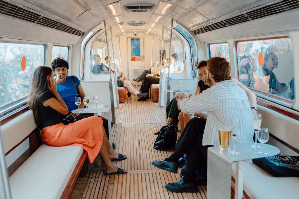 Interior of a modern boat or yacht with guests seated on benches, holding drinks and conversing.
