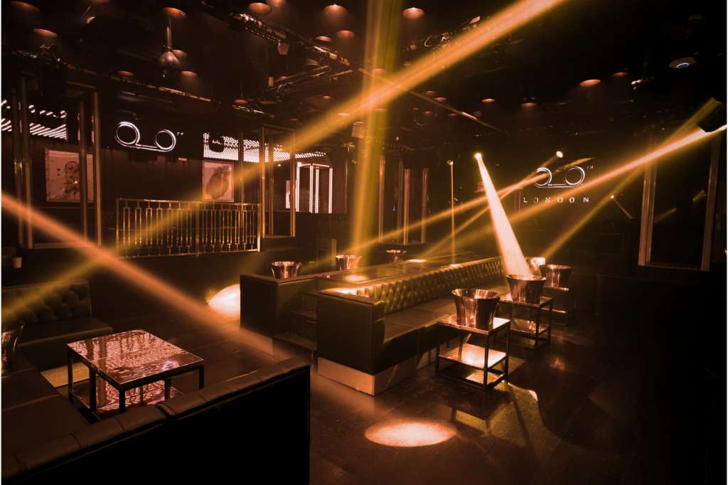 Modern event space with dramatic golden lighting, lounge seating, and neon signage on dark walls.
