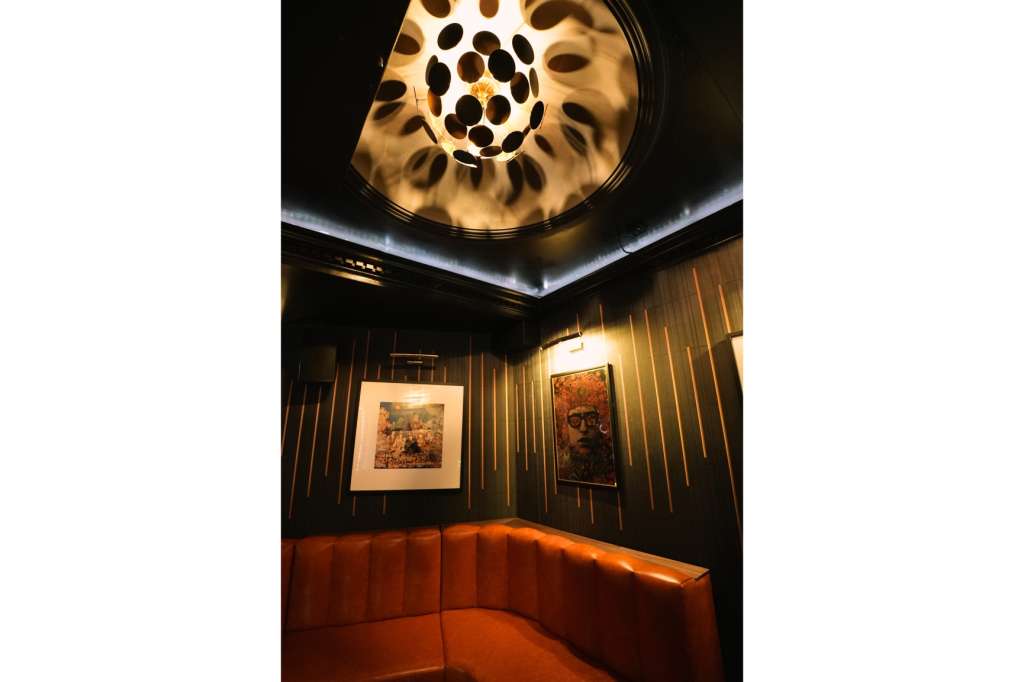 Dark interior room with curved orange seating, framed artwork on walls, and sculptural ceiling light fixture.