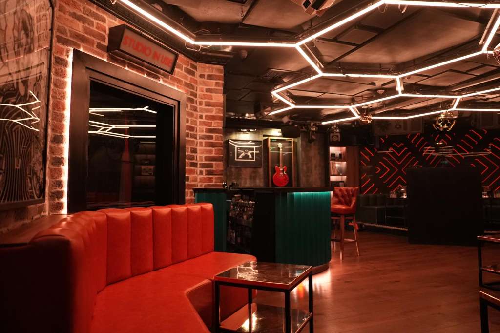 Modern lounge with red banquette seating, geometric neon lighting, exposed brick, and bar counter.