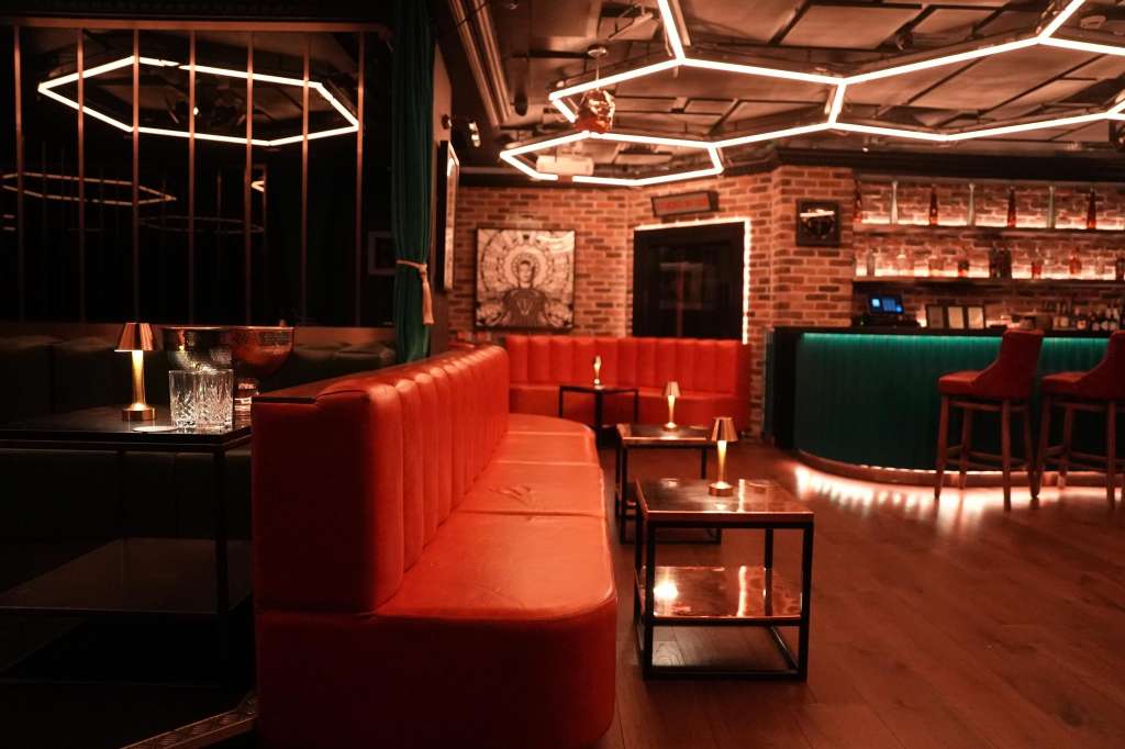 Modern lounge with red banquette seating, neon lighting, brick walls, bar counter, and candlelit tables.