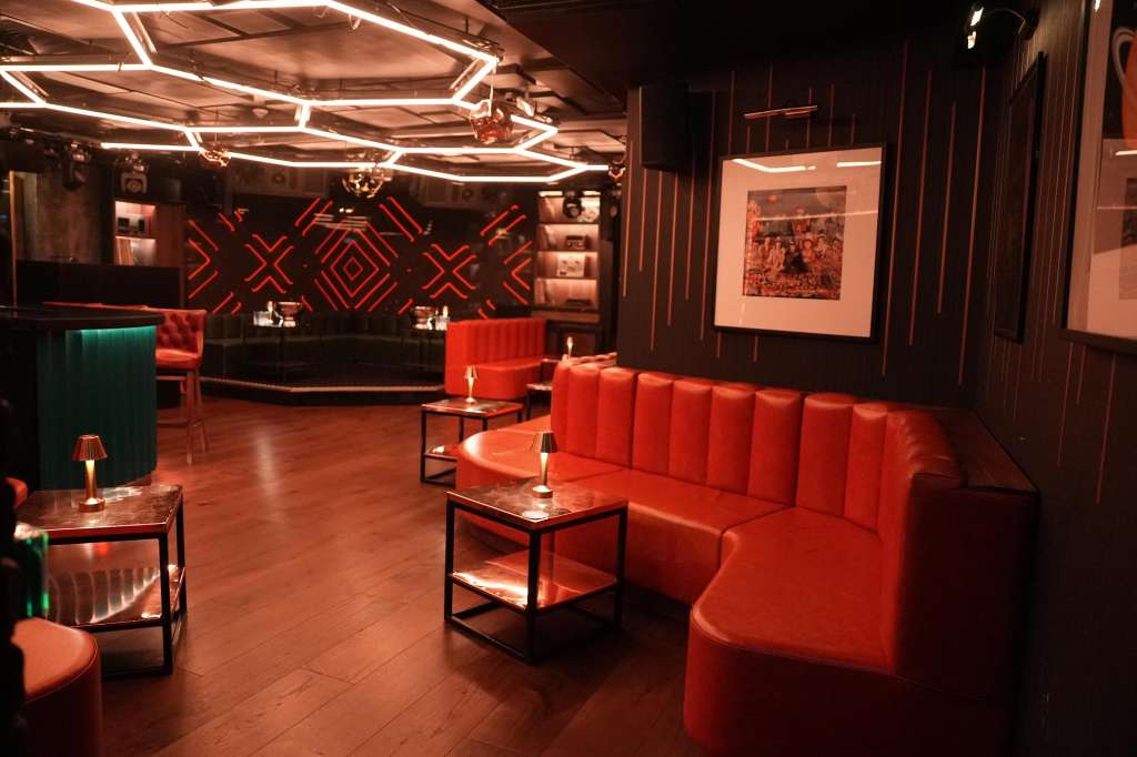 Main room with red neon lighting, geometric wall patterns, red banquette seating, and projection screens.