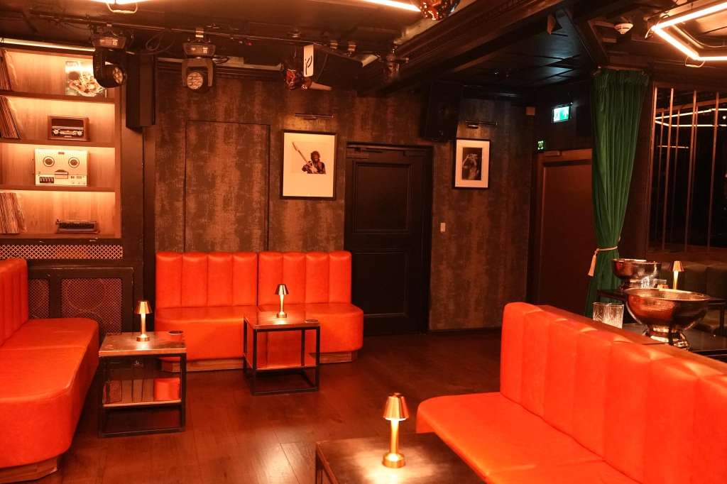 Main room with red velvet seating, warm ambient lighting, vintage decor, and bar area.