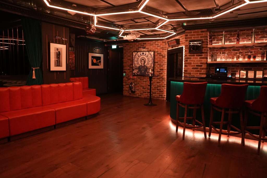 Modern event space with red curved seating, exposed brick walls, neon ceiling lights, and bar area with artwork displays.