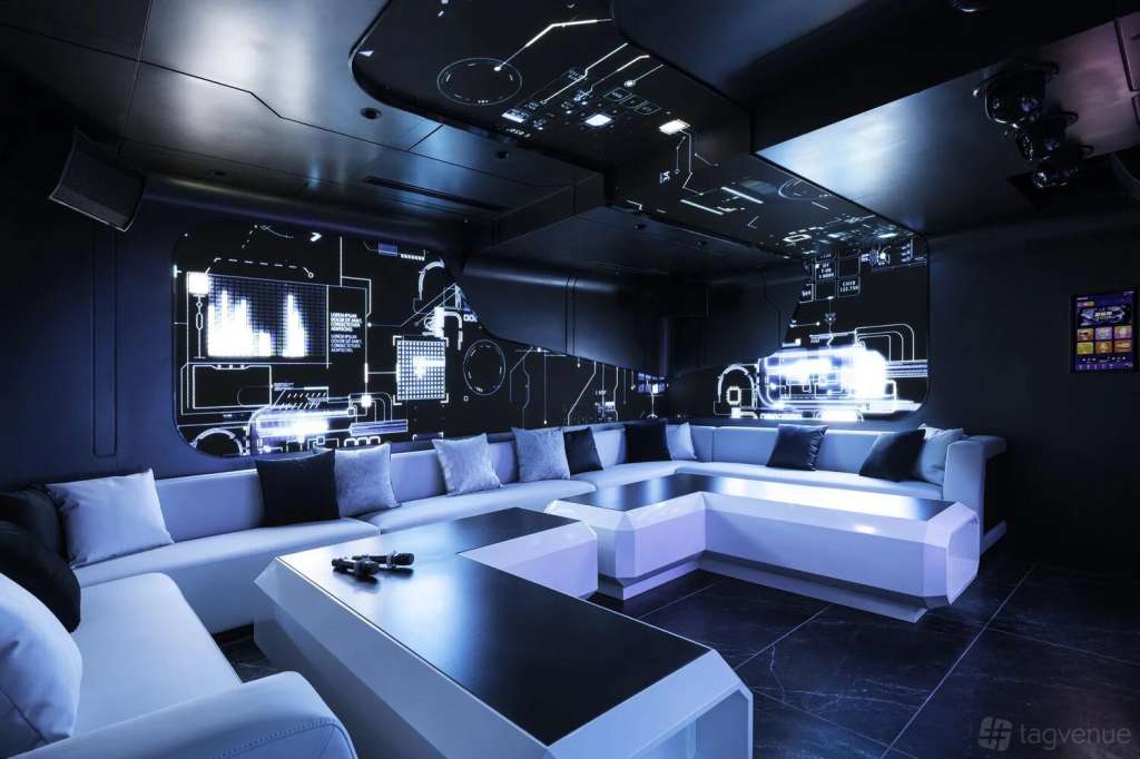 Modern karaoke lounge with white modular seating, neon signage, and professional audio-visual equipment on dark walls.