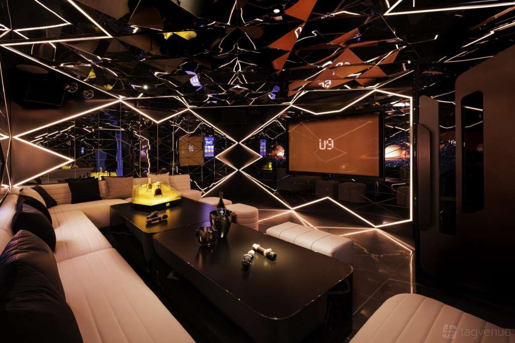 Modern lounge with geometric neon lighting, white seating, black tables, and large screen displaying u9 branding.