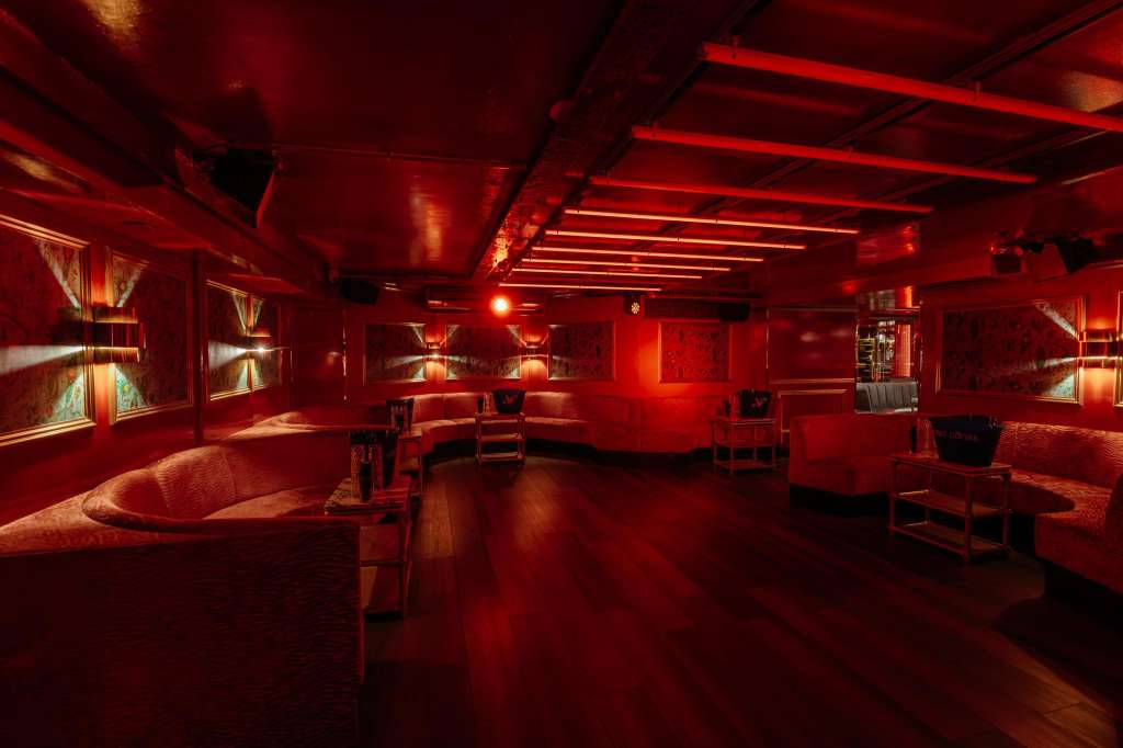 Modern interior with red ambient lighting, linear ceiling fixtures, lounge seating, and illuminated wall art.