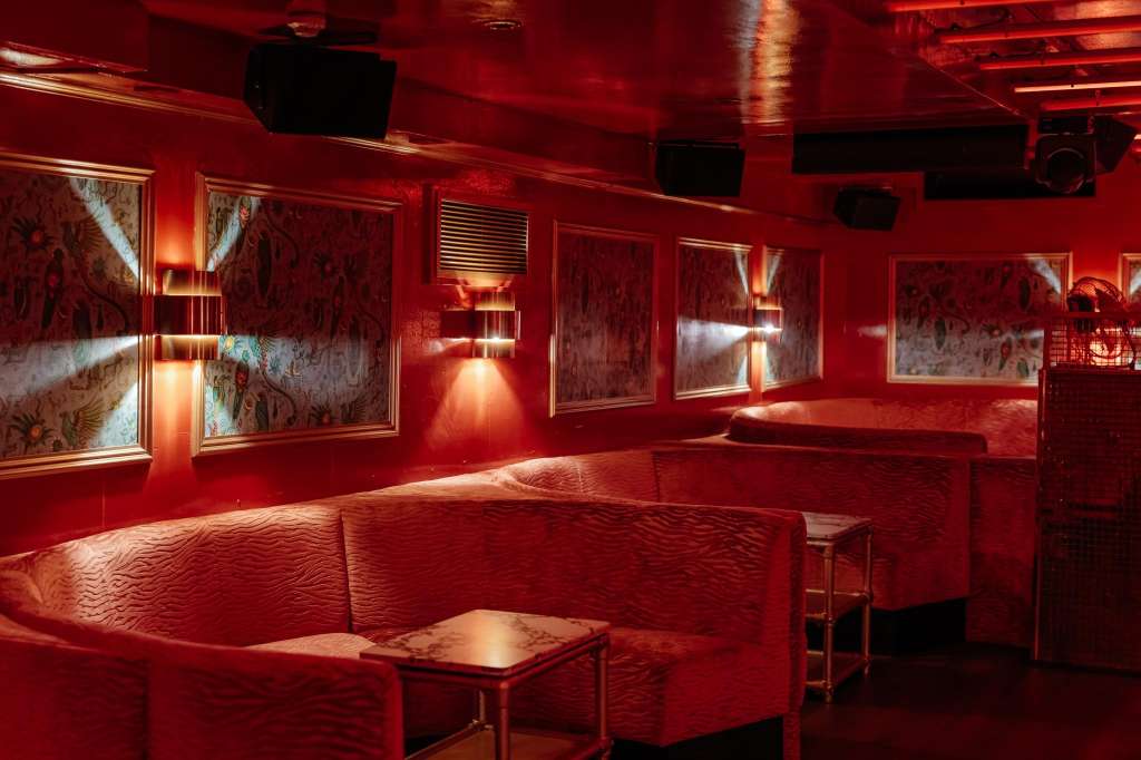 Red-lit lounge with curved seating, framed artwork on walls, and ambient uplighting.