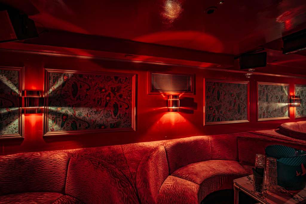 Interior lounge with red ambient lighting, framed artwork on walls, and red upholstered seating.