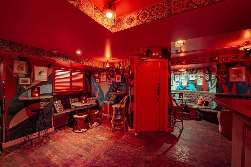 Main Room with red walls, decorative artwork, bar seating, lounge furniture, and ambient lighting.