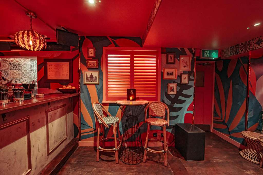 Main room with red neon lighting, bar counter, high-top seating, and contemporary wall art.