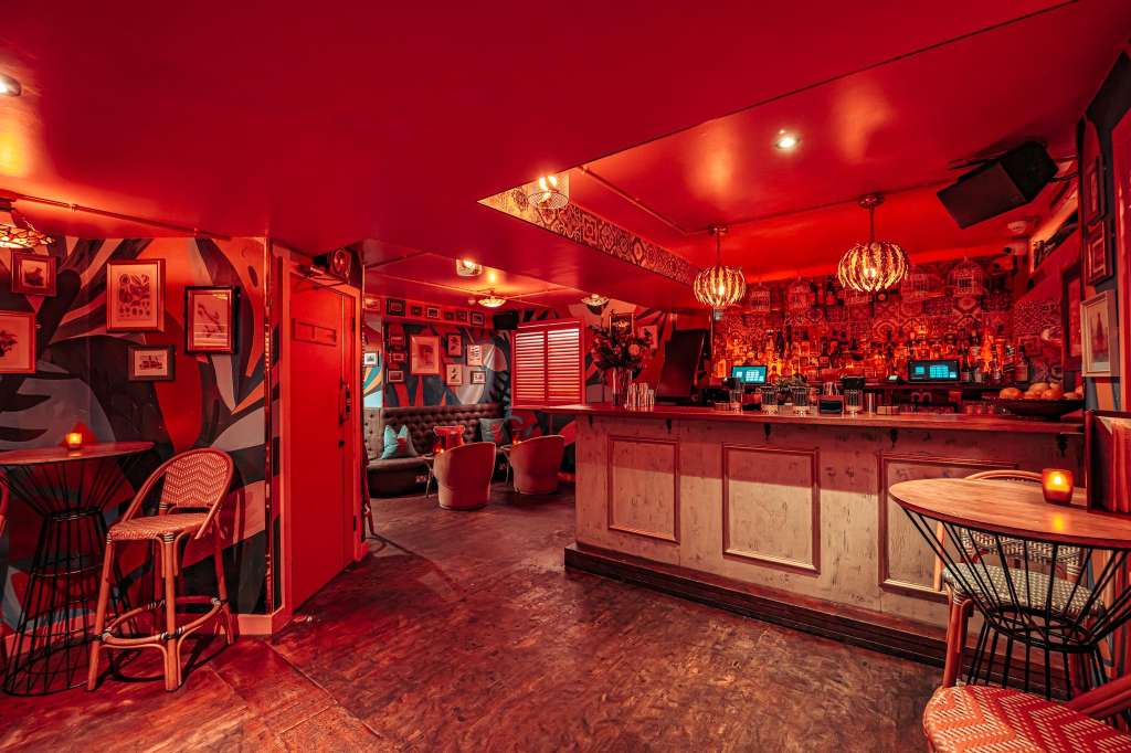 Main room with red ambient lighting, bar counter, lounge seating, decorative wall art, and pendant fixtures.