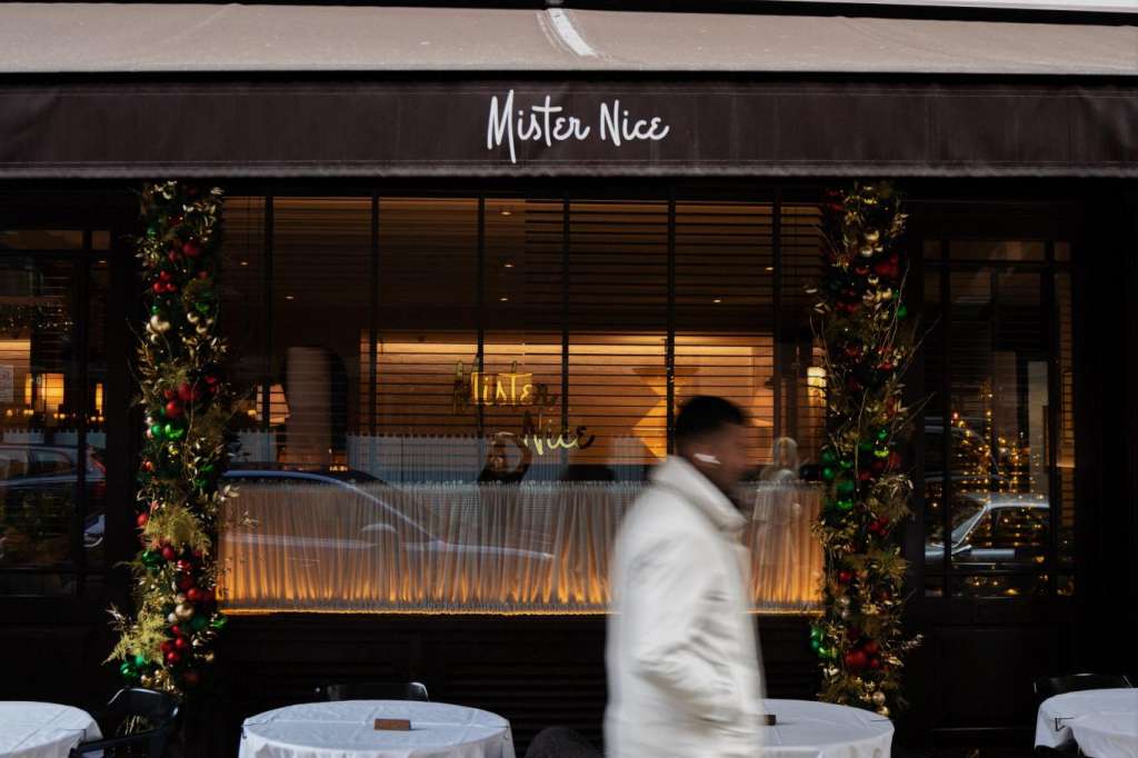 Mister Nice storefront with outdoor seating, white-clothed tables, black chairs, and festive garland decoration.