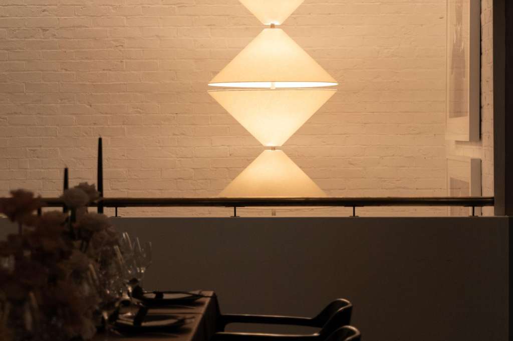Modern dining space with geometric pendant lighting, white brick wall, and place settings along a dark table.