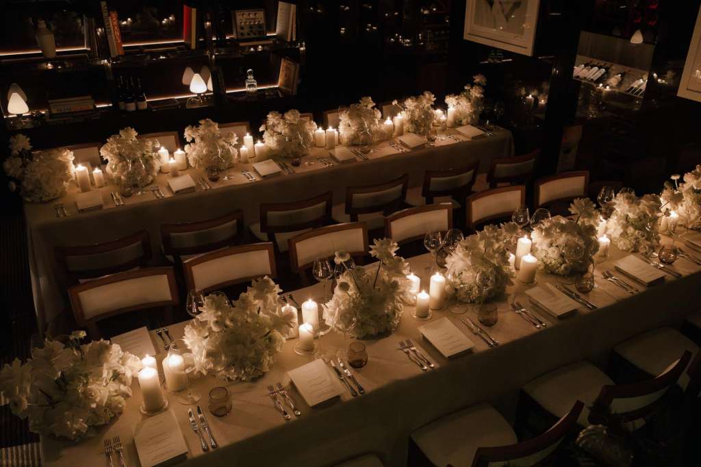 Long banquet table set for dinner with white floral centerpieces, candlelight, place settings, and formal table arrangement.