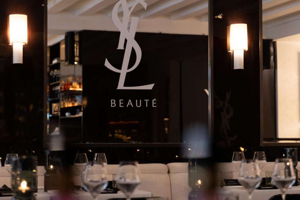 Dining room with long table set with glassware and place settings, branded backdrop with logo and exposed beam ceiling.